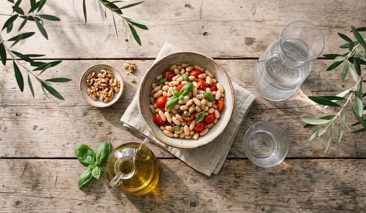 Gedeckter Holztisch im Abendlicht mit Bohnen, Tomaten, Walnüssen, Olivenöl und einer Wasserkaraffe statt Wein