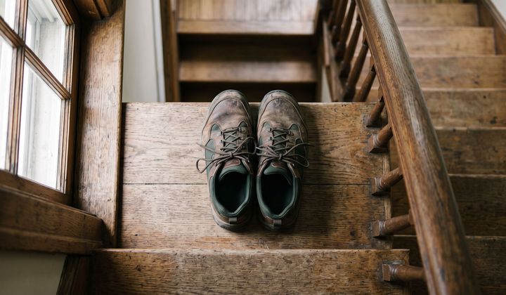 Ein Paar Laufschuhe auf einer Holztreppe neben dem Handlauf, im weichen Morgenlicht vom Fenster